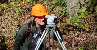Student in a hard hat looking into a surveying instrument